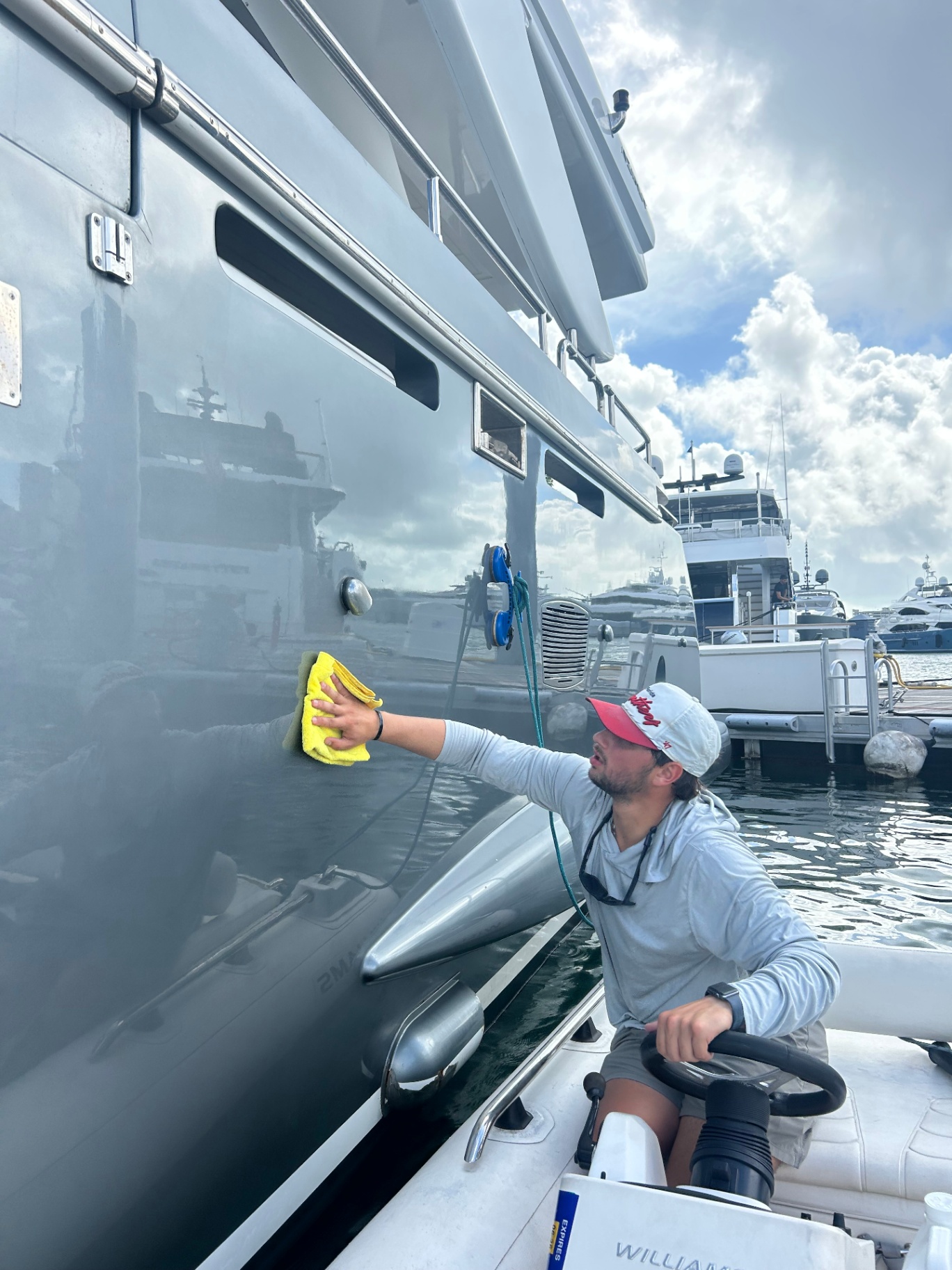 AC Detailing technician hand-polishing a superyacht hull from a tender